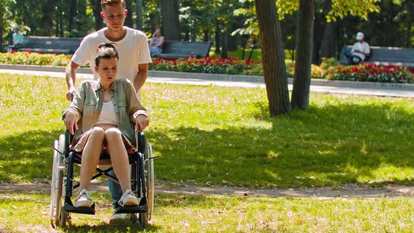 Friends in Park a Guy Rides Disabled Woman in a Wheelchair Then Stops and Sits Next to Her on the