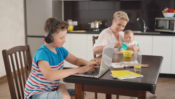 Boy Playing on Laptop While Woman Feeding Baby