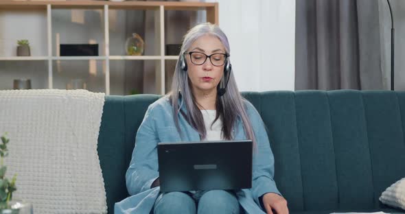 Senior Woman inHeadset Sitting in front of Laptop During Video Conference