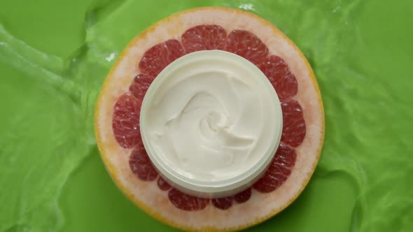 Cosmetic Jar of Moisturizing Cream on Piece of Red Citrus Fruit in Water Splash