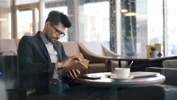 Entrepreneur Focused on Reading Book Sitting in Cafe Waiting for Meeting