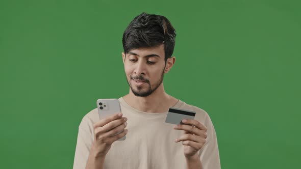 Happy Smiling Guy on Green Background in Studio Arab Man Pays Internet Order Using Phone and Credit