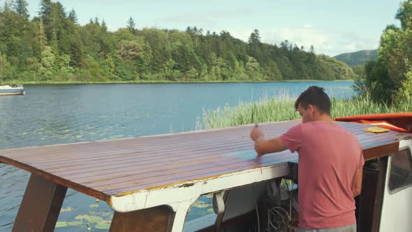 Young man brushing exterior protective paint wooden boat cabin roof