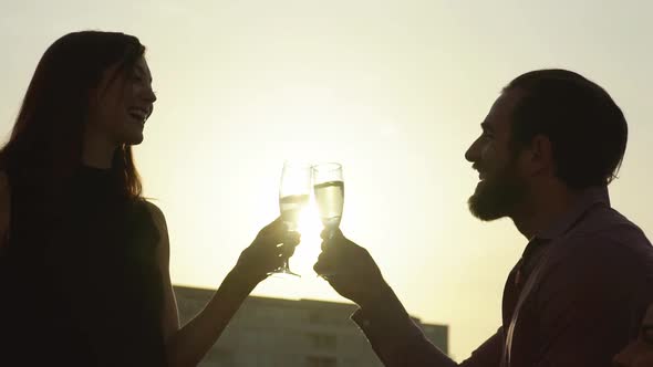 Slow motion shot of silhouetted couple clinking champagne glasses