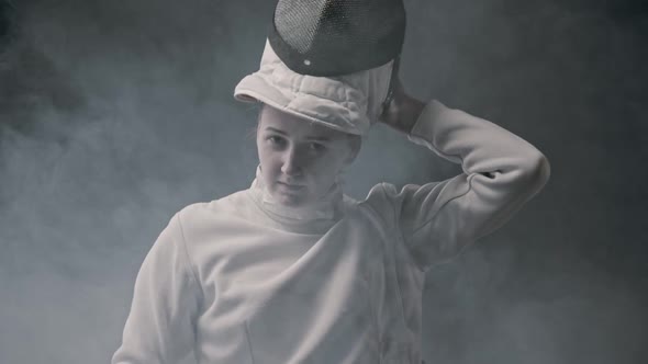 Fencing Training in the Smoky Studio - Young Woman Putting on a Helmet and Stands in the Position