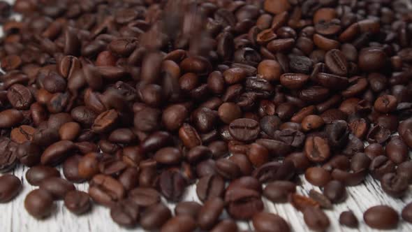 Mixed roasted Arabica and Robusta coffee beans slowly fall onto the vintage wood surface