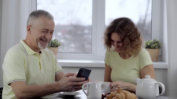 An Elderly Couple Laughs Merrily Looking at the Phone in the Kitchen