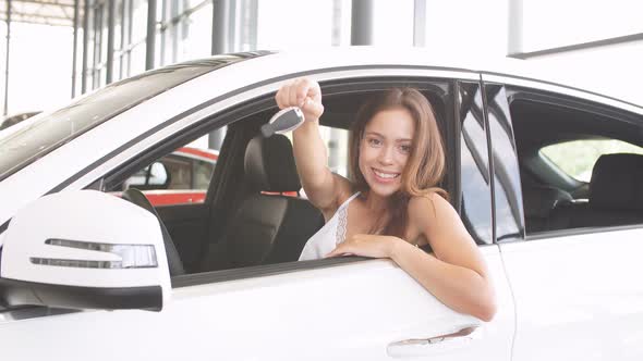 Happy Woman Driver in White Car Holds Car Keys in Her New Car at Car Show Room