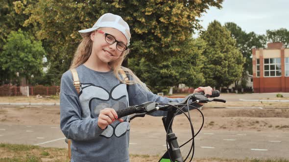 Blonde Little Girl Posing with Her Bicycle in the Summer in the City