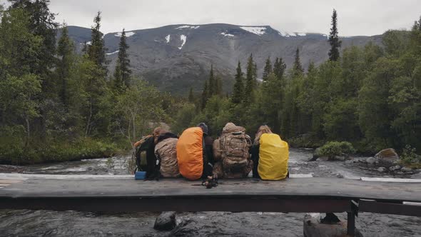 Group of Friends or Tourists Sitting on Bridge in Mountains Area and Having Rest