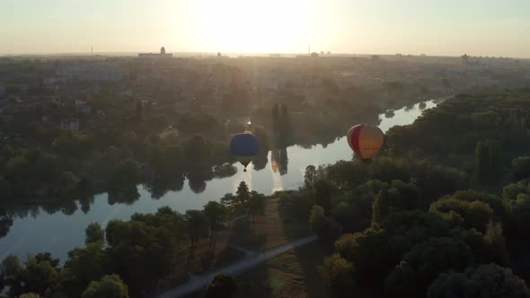 Beautiful flight at the sunrise of a red balloon over a river, forest, green trees.