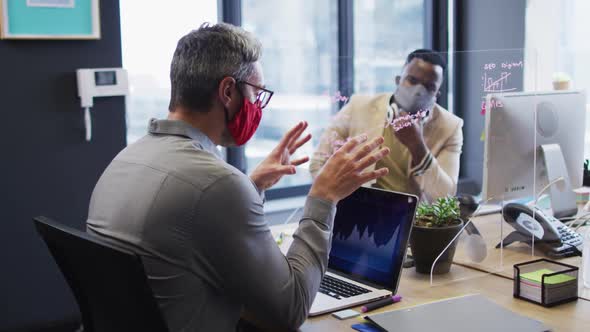 Diverse male office colleagues wearing face masks discussing at modern office