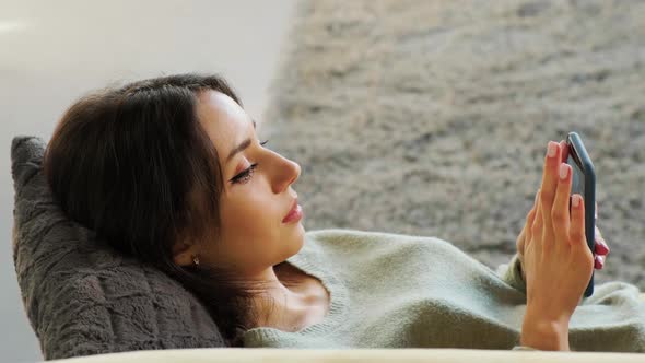 Woman Surf the Internet on Her Mobile While Relaxing on a Sofa in Her Living Room