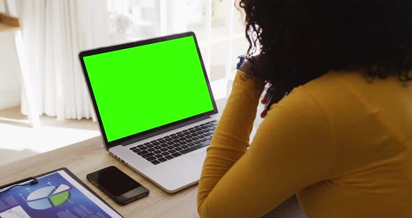 Rear view of african american woman looking at laptop with green screen while working from home