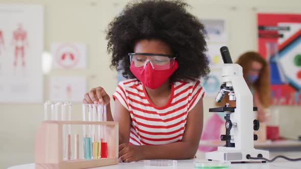 Girl wearing face mask and protective glasses using pipette and test tubes in laboratory