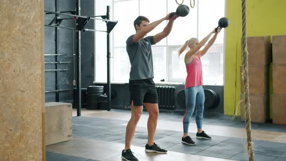 Slow Motion of Young Couple Exercising in Gym Squatting with Kettlebells Working Out