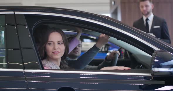 Side View of Young Happy Caucasian Family Sitting in Car Salon and Examining Interiors