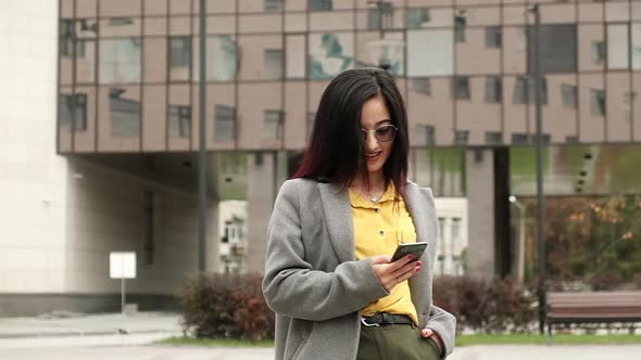 Stylish young woman uses modern phone on street to communicate and work in apps