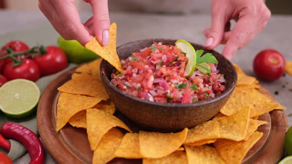 Woman Puts Nacho Chip Into Salsa Dip Sauce in Wooden Bowl