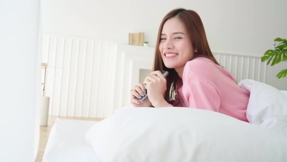 beautiful long hair asian woman nice smile enjoy smartphone chat after wakeup morning weekend on bed