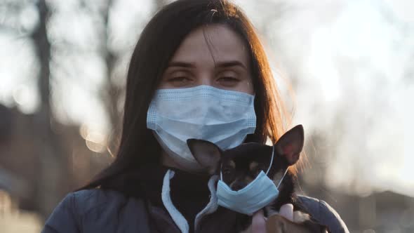 Woman in Protective Face Mask with Small Dog Wearing Medical Mask Too