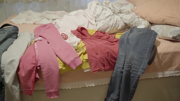 A messy bedroom. Lots of men and women clothes are thrown on a messy bed.