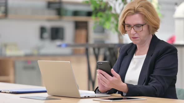 Old Businesswoman Using Smartphone and Laptop in Office