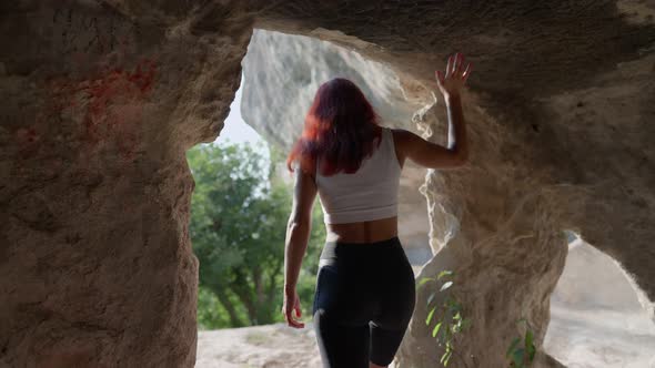 Slim Woman Traveler Dressed in Sportswear Walks Through Cave Moving Towards Exit