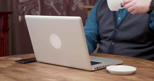 Man Drinks a Bit of Espresso While Working on His Laptop