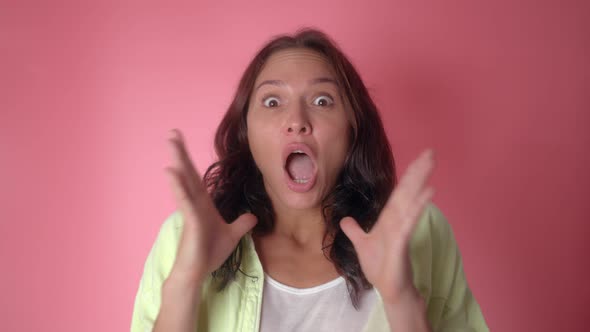 Shocked Woman Face with Opened Mouth and Eyes Looking to Camera on a Pink Wall Background