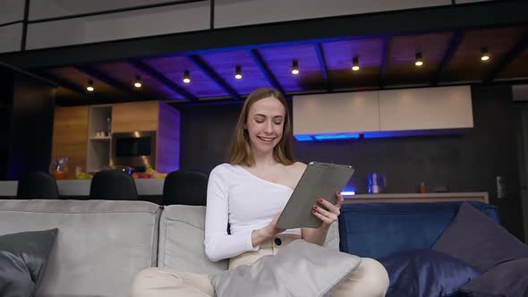 Girl in White Clothes which Sitting on the Sofa and Making Surprised Face During Working on i-pad