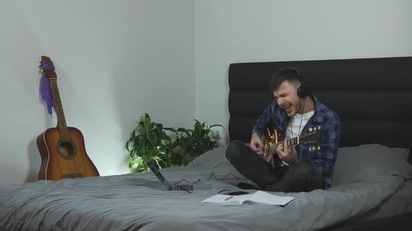 Guitar player in headphones playing on electric guitar on bed at home. Music concept