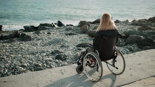 Disabled Woman Is Sitting in Wheelchair Near Sea Shore and Watching Waves