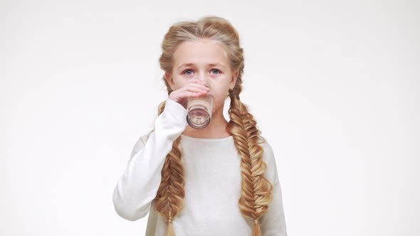 Young Adorable Caucasian Girl with Luxurious Long Blonde Hair Drinking Water From Glass on White