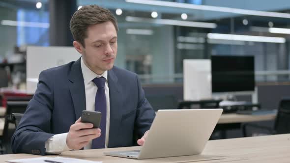 Businessman Using Smartphone While Using Laptop in Office