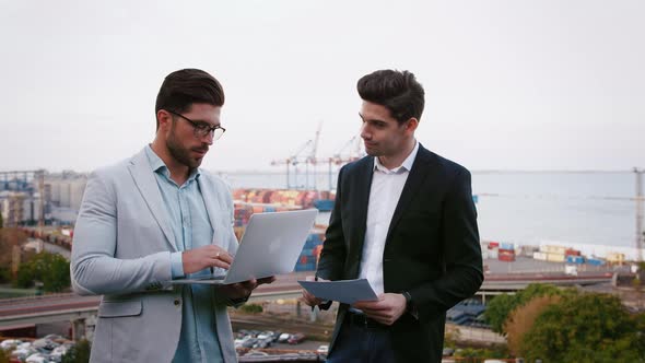 Two Business Partners Discussing the Meeting with Laptop and Contract Outdoors on Background of the