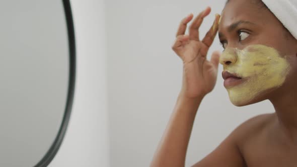 Happy african american woman apply beauty mask on face in bathroom