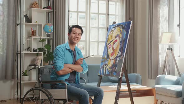 Asian Artist Man In Wheelchair Holding Paintbrush Turn And Crossing His Arms And Smiling