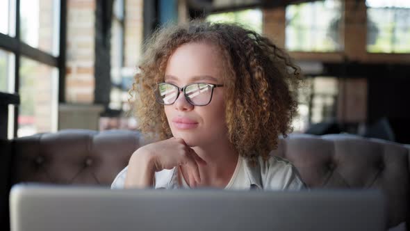 Girl in Glasses for Vision Looks Out Window While Working at Laptop