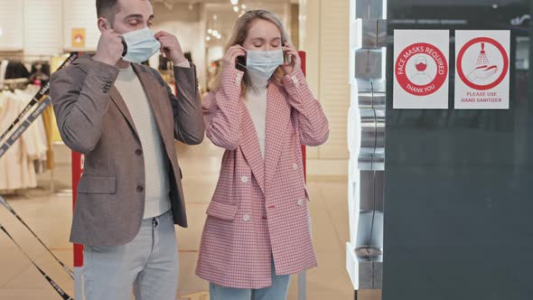 Couple Putting On Face Masks Before Entering Clothing Store