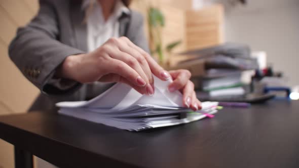 Closeup female hands of an office worker sorting through sheets from stack of documents.