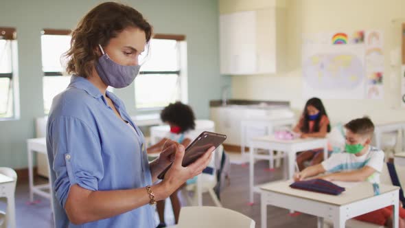 Female teacher wearing face mask using digital tablet at school