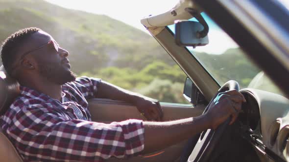 African american man with hands on steering wheel sitting in the convertible car on road