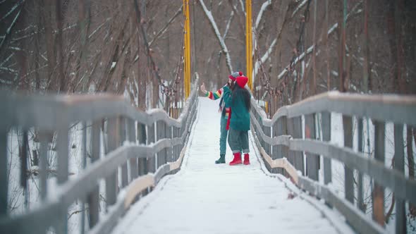 Two Young Women Friends in Colorful Clothes Taking Selfie on the Snowy Bridge