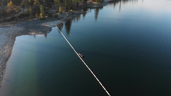 Aerial shot of a fishing boat near dam on a blue alpine lake surrounded by pine trees and mountains