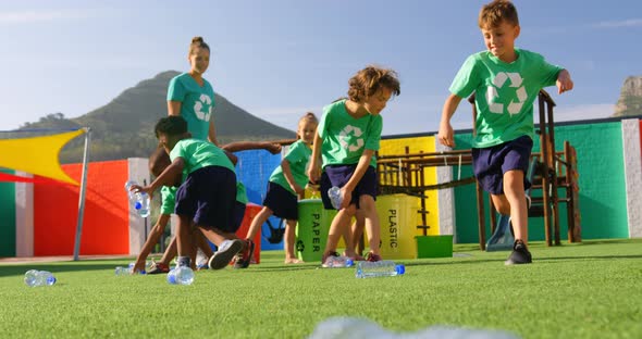 Front view of Caucasian female teacher teaching schoolkids about bottle recycle in the school playgr