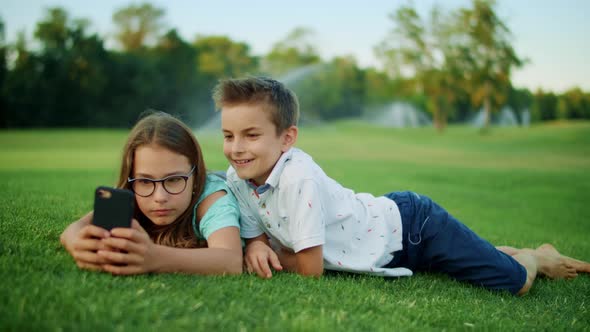 Brother and Sister Playing Games on Smartphone in Field. Kids Using Mobile Phone