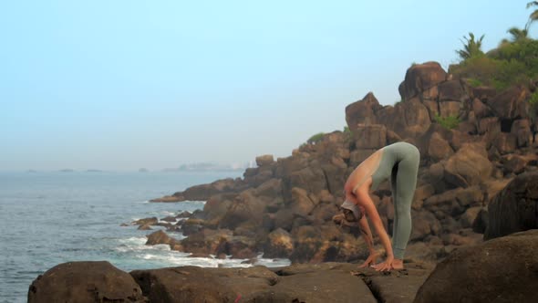 Pretty Lady Stands in Uttanasana Pose at Ocean Slow Motion