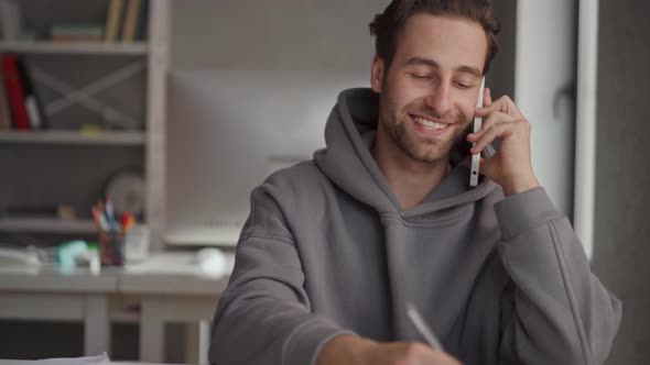 Concentrated man in hoodie talking by phone and reading papers