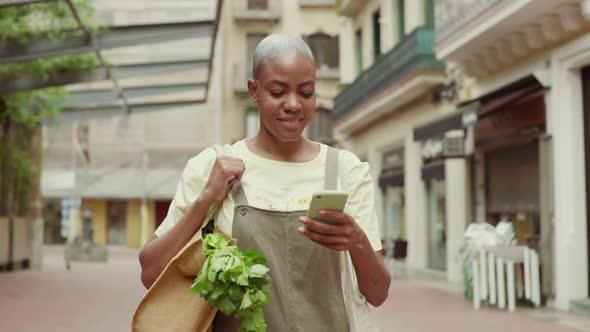 Slow motion shot of woman with grocery bag using smartphone in city